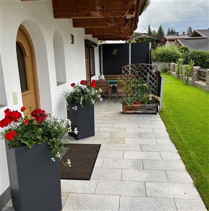An inviting entrance area with blooming plants in pots and a well-kept garden. The stone floor and the wooden paneling give the place a cozy atmosphere.