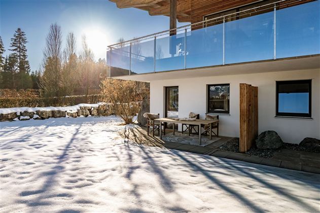 Ein schöner Esstisch im Freien, umgeben von Schnee. Die Sonne scheint auf die moderne Architektur des Hauses.