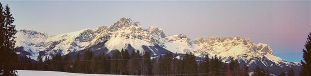 Eine beeindruckende Berglandschaft mit schneebedeckten Gipfeln und einem klaren Himmel. Die Wälder im Vordergrund vervollständigen das malerische Bild.