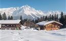 An idyllic winter scene with snow-covered cottages and majestic mountains in the background. The clear blue sky completes the peaceful atmosphere.