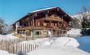 A traditional wooden house in the snow with a clear blue sky. The surroundings are covered by a white blanket of snow and a simple wooden fence.