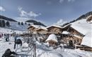 Ein malerisches Bergdorf mit Holzchalets im Schnee. Skifahrer genießen die winterliche Landschaft und die klaren Himmel.