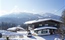 A snow-covered mountain village with traditional houses. In the background, majestic mountains rise under a clear blue sky.