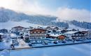 Een besneeuwd landschap met traditionele chalets en bergen op de achtergrond. De lucht is helder en de omgeving voelt rustig en uitnodigend aan.