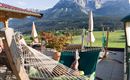 A terrace with a hammock and a view of the mountains. The surroundings are green and inviting, perfect for relaxing.