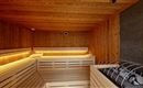 A modern sauna with wood paneling and gentle lighting. On the right side, the sauna stones are visible.