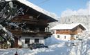 A snow-covered mountain village with traditional wooden houses.  
Children are playing in the snow in front of the houses.