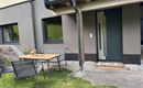 Eine moderne Haustür mit einem kleinen Vorplatz und einem Tisch mit Stühlen daneben. Der Bereich ist von einem gepflegten Garten umgeben.
