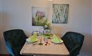An elegant dining area with a wooden table and two green chairs. On the table are decorated plates and flowers in a vase.