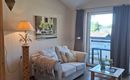 A cozy living space with a white sofa and a small table.  
Large windows let in a lot of light and provide a view outside.
