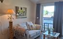 A cozy living room with a white sofa and a floor lamp. Large windows let in plenty of natural light.
