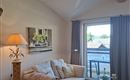 A cozy living room with a beige sofa and a floor lamp. Large windows offer a view outside and bring a lot of light into the room.