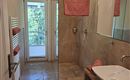 A modern bathroom with a shower and a wash basin. The walls are painted in neutral colors, and there are orange towels.