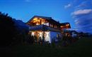 A beautiful house in the evening light, surrounded by greenery. The sky has a gentle twilight with some clouds.