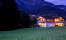 A stylish house in the mountains at twilight, surrounded by meadows. The warm lights of the house shine into the peaceful landscape.