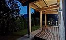 A cozy porch with a wooden ceiling under a clear night sky. Nearby, plants and trees are visible.
