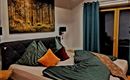 A cozy bedroom with a large bed and modern pillows. The wooden beam ceiling and the artistic picture on the wall give the room a warm atmosphere.
