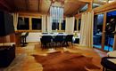 A modern living room with wooden floors and large windows. The space is elegantly furnished and features a dining area with a table and chairs.