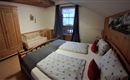 Ein gemütliches Schlafzimmer mit einem Doppelbett und einem Babybett. Die Wände sind aus Holz und das Zimmer hat große Fenster mit Vorhängen.
