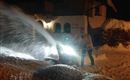 A snowplow is clearing snow at night in front of a house. The snow is being pushed away with bright light.