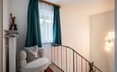 An inviting hallway with a cozy seating area and a window. The walls are light, and the space is accented by a modern lamp and beautiful curtains.
