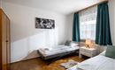 A simple bedroom with two single beds and a bright atmosphere. Large windows and green curtains create a cozy space.