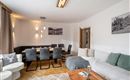 A modern living room with a cozy couch and a dining table for twelve people. The walls are painted light and a large window ensures plenty of light.