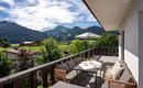 A beautiful terrace with comfortable furniture and a magnificent view of green mountains. The sky is clear and the landscape is idyllic.