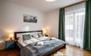 A modern bedroom with a large bed and soft colors. Windows with curtains let in plenty of light and create an inviting atmosphere.