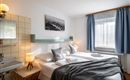 A cozy bedroom with a double bed and two pillows. The room has large windows and a calm, friendly atmosphere.