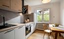 Modern kitchen with wooden and white elements. A table with fruit and large windows creates a bright, welcoming atmosphere.