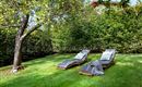 Two loungers are positioned on a green meadow, surrounded by trees and shrubs. Sunshine and a calm atmosphere invite relaxation.