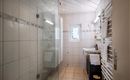 A modern bathroom with a glass shower and bright tiles. On the wall, there is a towel warmer, and a large window provides daylight.