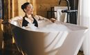 Eine Frau entspannt in einer modernen Badewanne mit Schaum. Der Raum hat warmes Holz und sanfte Beleuchtung.