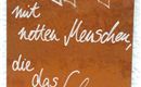 Ein rostiger Schild mit handgeschriebenem Text. Der Spruch beschreibt die Bedeutung von Begegnungen mit netten Menschen im Leben.