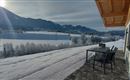 Eine schneebedeckte Landschaft mit Bergen im Hintergrund. Auf der Terrasse stehen ein Tisch und Stühle, ideal zum Entspannen.