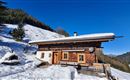 An idyllic mountain cabin in the snow, surrounded by forests and mountains. The blue sky and the snowy landscape create a relaxed winter atmosphere.