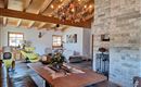Een gezellige woonkamer met houten plafonds en een grote eettafel. De inrichting is modern met rustieke elementen en een mooie steenwand.