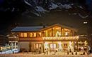 Eine gemütliche Berghütte im Schnee mit festlicher Beleuchtung. Im Hintergrund sind beeindruckende Berge zu sehen.