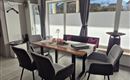 Ein moderner Essbereich mit einem Holz-Tisch und vier grauen Stühlen. Große Fenster lassen viel Licht herein und bieten einen Blick auf die Außenansicht.