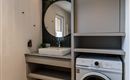 A modern washroom with a washing machine and a large mirror. The walls are bright, and the room is clean and neatly designed.