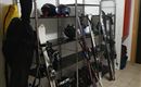Ein Skiraum mit Regalen, auf denen Skiausrüstung, Helme und Skier aufgereiht sind. Die Wände sind neutral und der Boden ist gefliest.