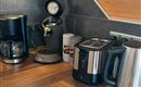 A modern kitchen corner with a coffee machine, a kettle, and a toaster. The wooden countertop gives the scene a cozy atmosphere.