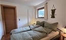 Ein gemütliches Schlafzimmer mit zwei Einzelbetten und Holzboden. Die Wände sind hell gestrichen und ein Fenster sorgt für Tageslicht.