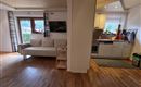 Ein helles Wohnzimmer mit einer bequemen Couch und einem Fernseher. Die angrenzende Küche ist modern und gut ausgestattet.