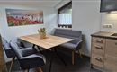 A cozy dining area with a wooden table and modern chairs. On the wall, there is a picture of a beautiful landscape with flowers.