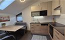 A modern kitchen with wooden shelves and light walls. The room has a large window and a small dining area with a table and chairs.