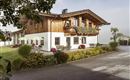 A charming house in alpine style with wooden cladding and a balcony. Surrounded by green meadows and blooming plants.