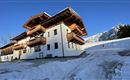 A modern building in alpine style, surrounded by snow and mountains. The balconies are made of wood, giving the house a cozy charm.