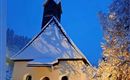 Eine kleine Kapelle im Schnee bei Dämmerlicht. Die Bäume sind mit Schnee bedeckt und die Umgebung strahlt eine ruhige Winteratmosphäre aus.